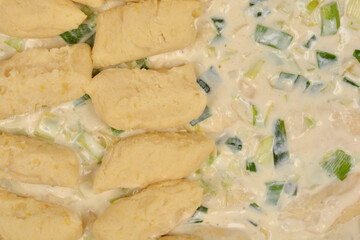 Raw homemade potato gnocchi are resting in a rich cream, leek, and onion sauce, ready to be baked.