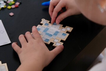 A girl makes a Christmas toy with her own hands from ceramic mosaic. Ceramic mosaic, DIY Christmas tree toy. Eco-friendly toy, educational activity for children.