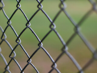 Fototapeta premium Close-Up of Chain Link Fence with Shallow Depth of Field - Metal Wire Mesh Barrier with Blurred Green Background