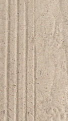Close-up of textured sand with visible lines and patterns. The surface appears smooth and light beige in color, showcasing natural elements