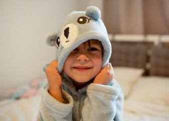 Cute child in a soft blue bathrobe with bear ears smiling after bath time, sitting on the bed. Concept of childhood, hygiene, comfort, and family care.