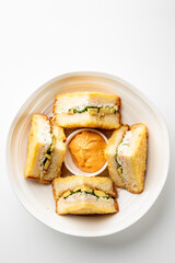 Assorted sandwich halves with cucumber, avocado, and creamy filling arranged around dipping sauce on white plate, top view, isolated on white background, suitable for food photography.