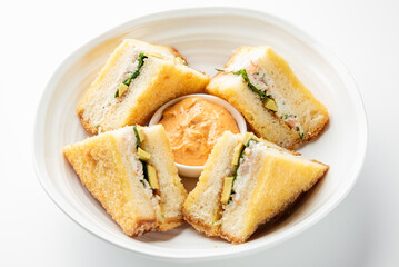 Assorted sandwich halves with cucumber, avocado, and creamy filling arranged around dipping sauce on white plate, top view, isolated on white background, suitable for food photography.