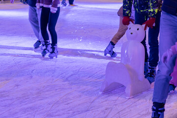 Fototapeta premium people ice skating on a winter rink with a polar bear skating aid under colorful lights during evening