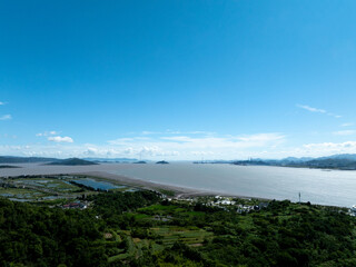 Aerial view of a coastal area with lush greenery, water, and distant islands