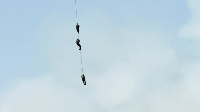 Three military paratroopers in the air against the sky descend into a landing rope. Demonstration performance. Copy space for text