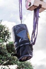 A black industrial bag secured with straps and suspended by a crane hook