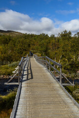 Two backpackers walking on the wooden bridge over the Storulvån river, starting point for a Jämtland triangle hiking backpacking trail.