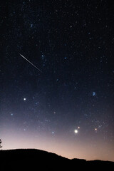 Obraz premium Milky Way stars with meteor shower trails and countryside silhouettes.