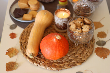 Lit candles, cookies, chocolate, nuts, tea, wine, pumpkins, books, reading glasses and autumn leaves on the table. Autumnal hygge at home. Selective focus.
