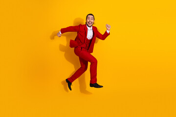 Funny energetic man in red suit leaps across a bright yellow background for a bold stylish moment and celebration of fashion and joy