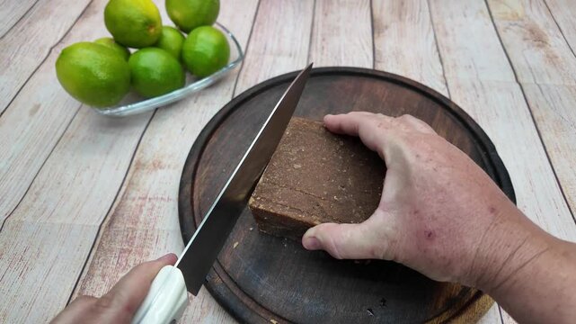 close-up shot hands using a knife to slice a block of panela on a rustic wooden board, ready for a sweet recipe sugar cane limeade