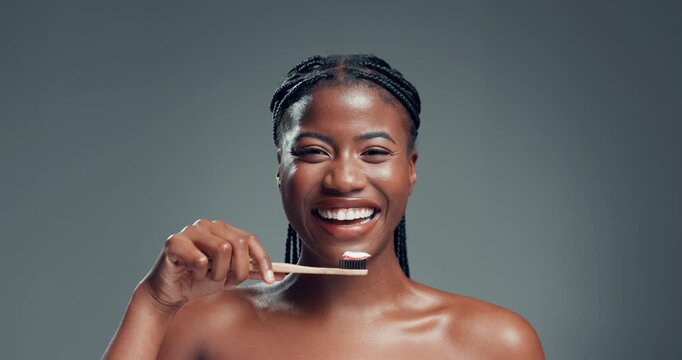 Oral health, toothbrush and face of black woman in studio with routine for fresh breath. Happy, toothpaste and portrait of African person brushing teeth for dental care and hygiene by gray background