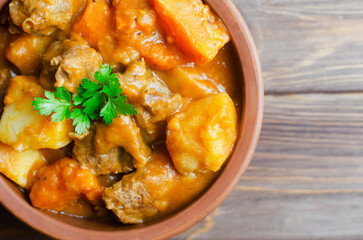 Goulash stew of stewed veal and vegetables with a feather in a ceramic bowl on a wooden background. Traditional Hungarian cuisine concept. Horizontal orientation. Selective focus. Top view. Copy space