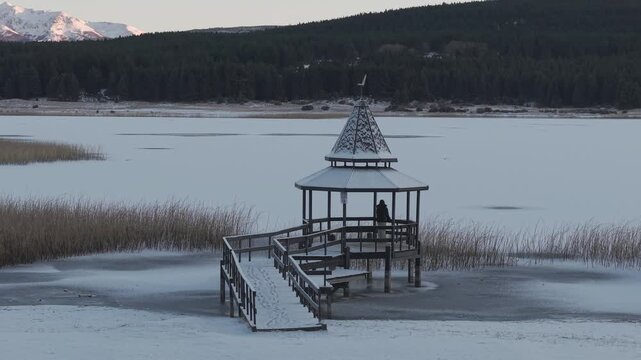 Woman standing on wooden pier by frozen Laguna La Zeta with snowy mountains in Patagonia.