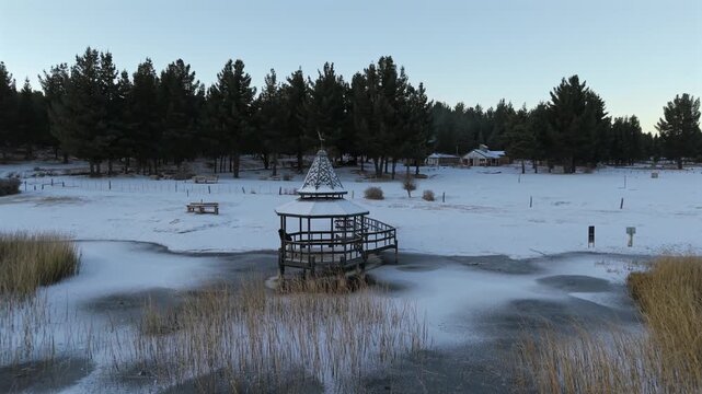 Drone orbiting snowy pier on frozen Laguna La Zeta with lonely woman gazing in silence.