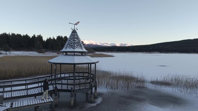 Woman walking on snowy pier overlooking frozen Laguna La Zeta with mountains in the distance.