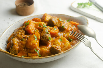 Goulash stew of stewed veal and vegetables with a feather in a white bowl on a white background. Concept of traditional Hungarian cuisine. Horizontal orientation. Selective focus. Top view.