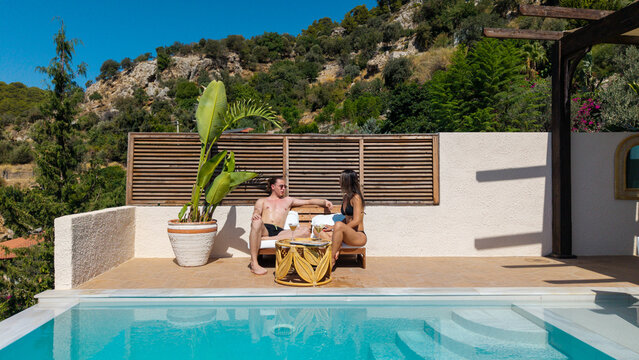 Idyllic Oasis: A couple enjoys a serene moment by the pool, soaking up the tranquil atmosphere. Embracing the beauty of the outdoors, while enjoying the refreshing waters. 