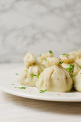 Boiled khinkali on a ceramic plate on a wooden table. Minimalism style. Traditional Georgian cuisine concept. Vertical orientation. Selective focus. Copy space