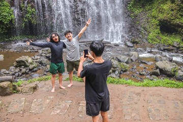 Obraz premium Friends Capture Joyful Memories At Stunning Waterfall During Tropical Vacation Adventure