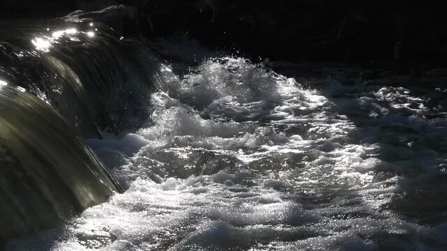 Sunlight sparkling on water cascading over a dark ledge