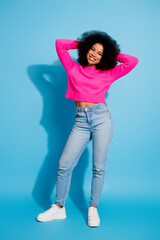 Obraz na płótnie Canvas Young stylish female in vibrant pink sweater and casual jeans posing on a blue background with charm and confidence