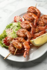 Skewers with tasty grilled shrimps, salad and lemon slice on white marble table, closeup. Delicious seafood dish