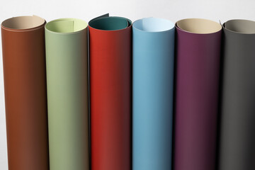 a row of colorful, rolled materials, like paper or synthetic leather, featuring rich tones: brown, sage, red, teal, aubergine, and charcoal gray