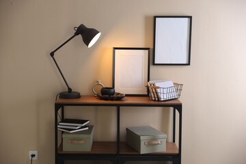 Stylish lamp, other decor and books on console table near beige wall indoors