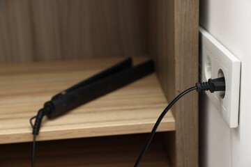 Hair straightener plugged into power socket indoors, closeup
