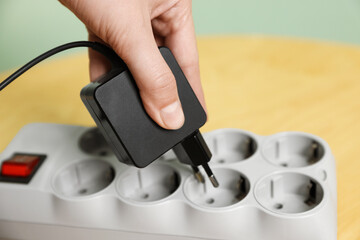 Woman plugging USB adapter with cable into power strip at table, closeup