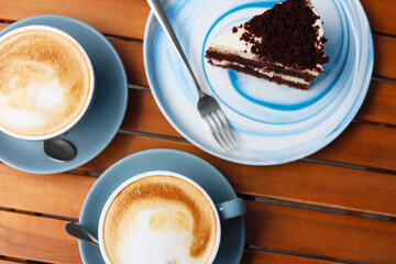 Cups of aromatic coffee and slice of cake on wooden table, flat lay