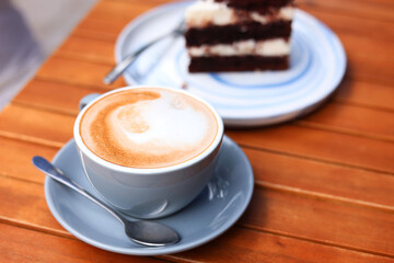 Cup of aromatic coffee and slice of cake on wooden table, closeup