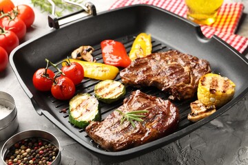 Pan with grilled beef steaks, mushrooms, vegetables and spices on grey textured table, closeup