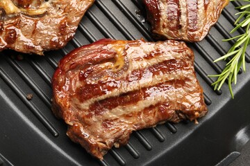 Grilled beef steaks and rosemary on black pan, top view