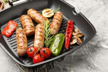 Pan with grilled sausages, vegetables, mushrooms and spices on gray textured table, closeup
