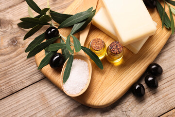Handmade soap bars, olives, green leaves, sea salt and essential oils on wooden table, top view