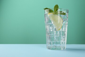 Refreshing water with lemon, mint and ice on table against turquoise background. Space for text