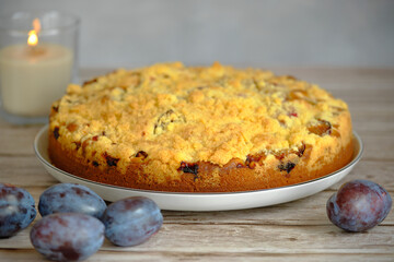 Close-up of homemade pie with plum crumbs, still life with berries on a wooden table and a candle in the background background.