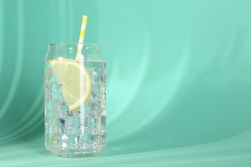 Refreshing water with lemon and ice on turquoise background. Space for text