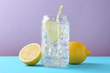 Refreshing lemon water with ice in glass and fresh citrus fruits on color background, closeup