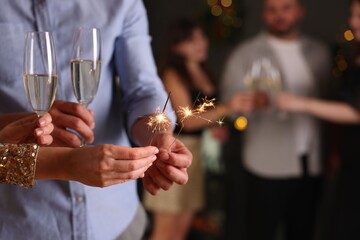 Friends celebrating New Year with sparklers and wine glasses indoors, closeup
