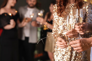 Friends celebrating New Year with sparklers and wine glasses indoors, closeup