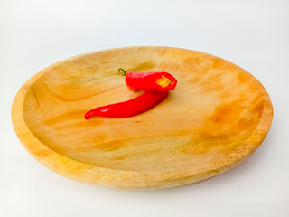 Whole red chili pepper cut in half, served on a wooden plate, isolated on a white background.