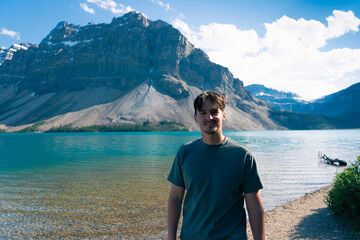 Man smiles by a tranquil lake with mountains in the background