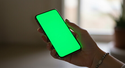 Elegant hand holding modern smartphone with vibrant green screen for creative content