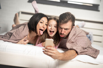 Young parents making funny facial expression and taking selfie with smart phone
