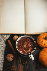 Cozy autumn scene with mug of hot chocolate, pumpkins and empty notebook with copy-space on rustic dark wooden background, warm seasonal atmosphere
