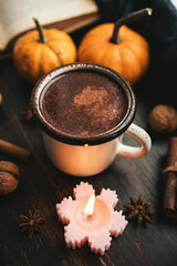 Cozy autumn scene with mug of hot chocolate, book, pumpkins, spices and candles on rustic dark wooden background, warm seasonal atmosphere